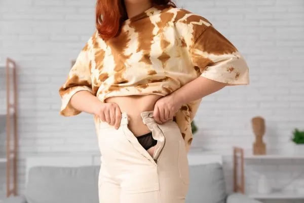 Image of woman trying to do her trousers up after pregnancy weight gain Glossop